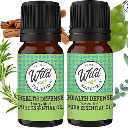 Two bottles of Wild Essentials Health Defense Pure Essential Oil with green labels and black caps, surrounded by herbs on a white background.