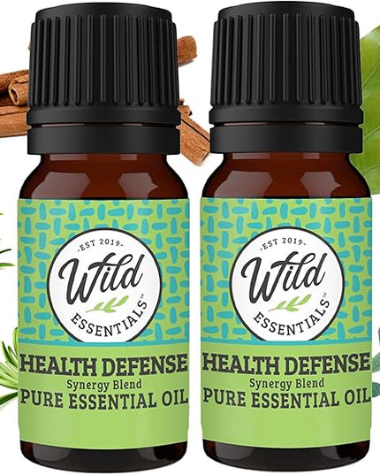 Two bottles of Wild Essentials Health Defense Pure Essential Oil with green labels and black caps, surrounded by herbs on a white background.