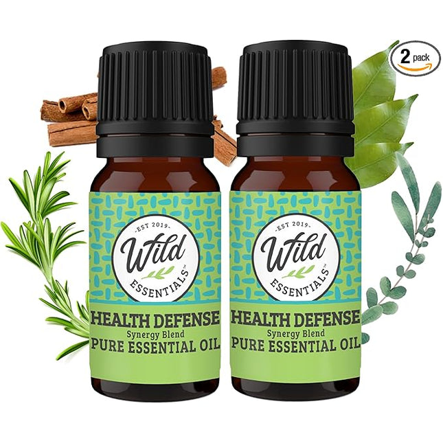Two bottles of Wild Essentials Health Defense Pure Essential Oil with green labels and black caps, surrounded by herbs on a white background.