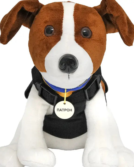 Plush dog toy with a black harness and name tag on a white background
