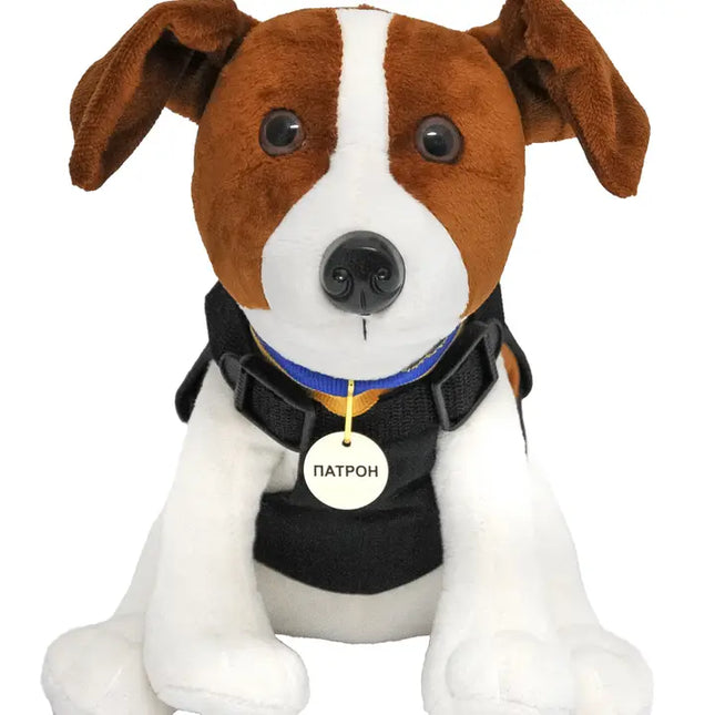 Plush dog toy with a black harness and name tag on a white background
